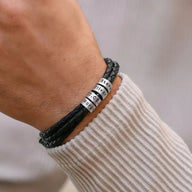 Bracelet triple tour en cuir noir tressé avec quatre anneaux métalliques gravés sur poignet homme.