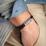 Bracelet homme en cuir noir triple tour avec cinq anneaux métalliques gravés sur poignet.