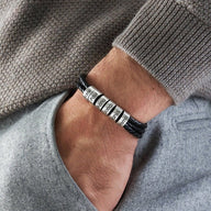 Bracelet triple tour en cuir noir avec six anneaux métalliques gravés porté au poignet.