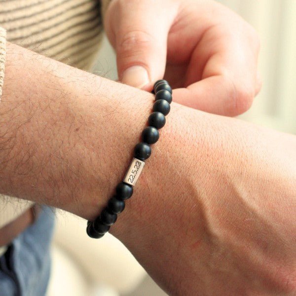 Bracelet mixte en pierres naturelles noires mat avec perle en métal gravée porté au poignet.