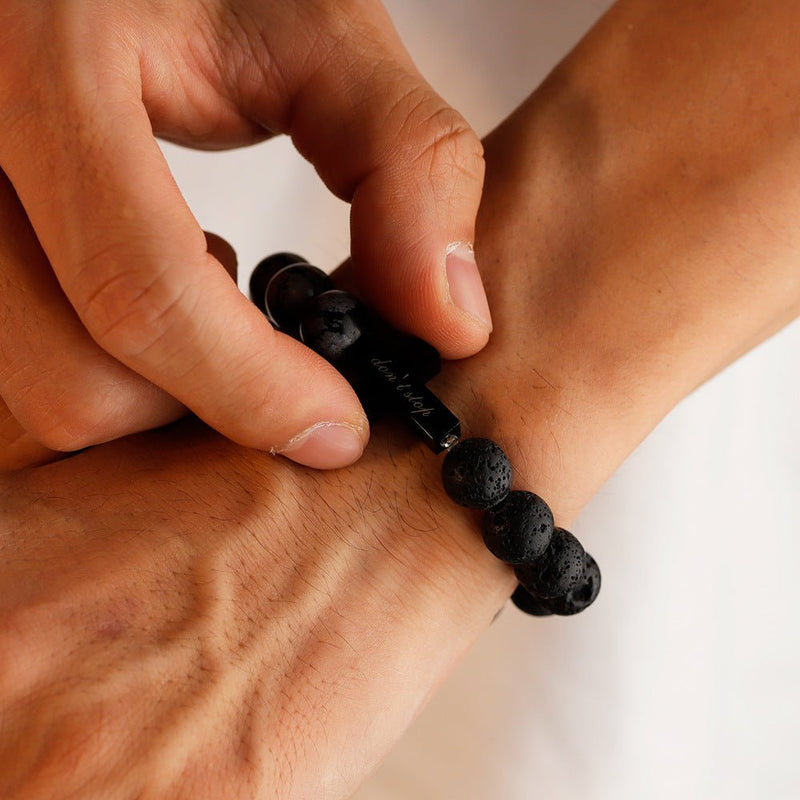 Bracelet masculin avec perles noires volcaniques et turquoise, croix gravée centrale en métal, style moderne et affirmé.