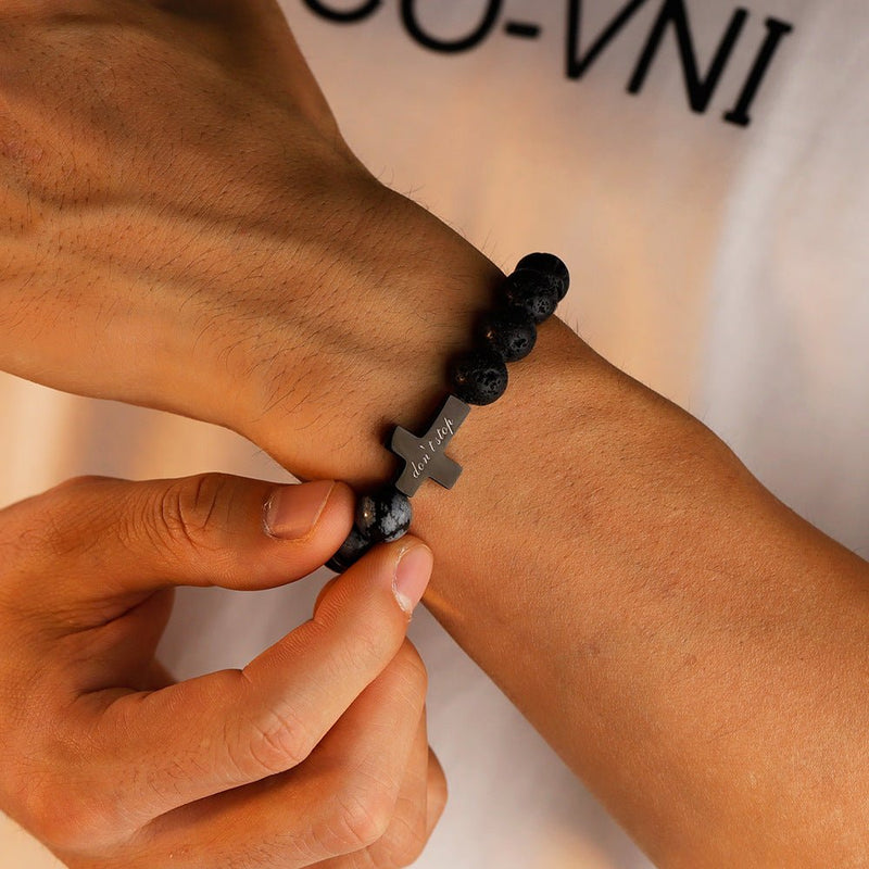 Bracelet homme en perles noires de pierre volcanique avec croix gravée centrale en métal gris anthracite.