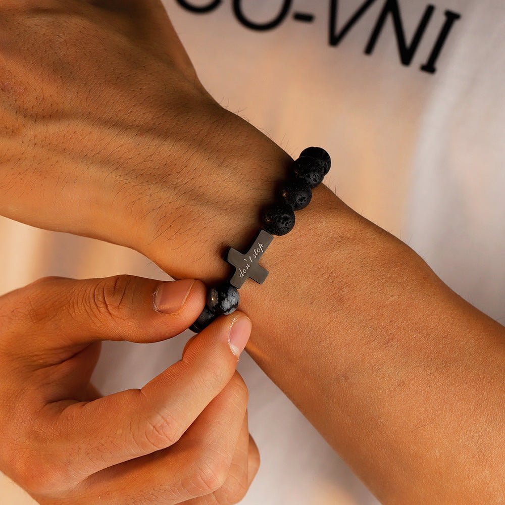 Bracelet homme en perles noires de pierre volcanique avec croix gravée centrale en métal gris anthracite.