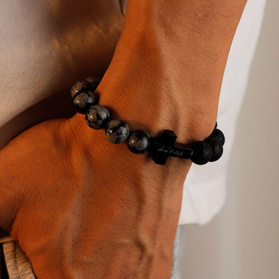 Bracelet homme perles noires mate et brillantes en pierre volcanique, détail croix gravée en métal noir, style masculin.