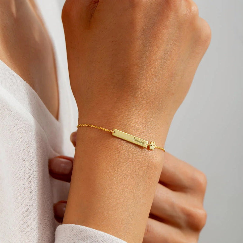 Bracelet fin en acier inoxydable doré avec plaque rectangulaire gravée, chaîne délicate et fermoir ajustable.