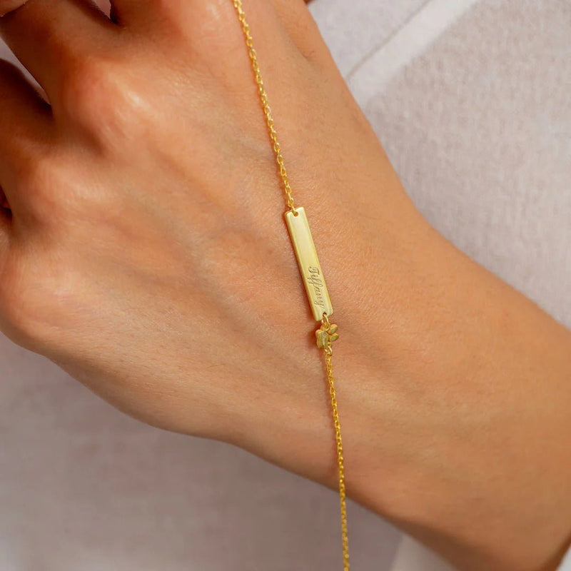 Bracelet fin en acier inoxydable doré avec plaque gravée et petit pendentif patte d’animal délicat.