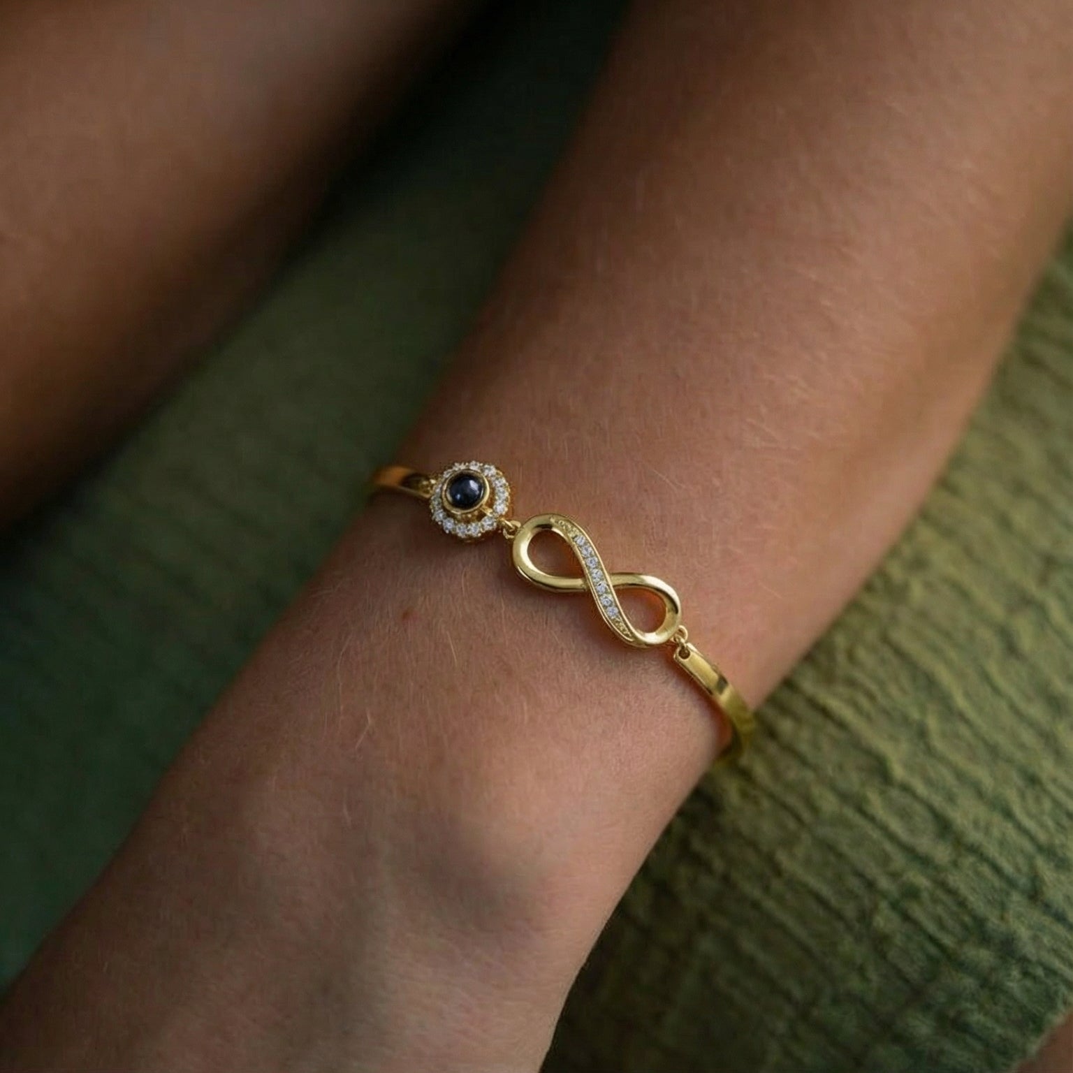 Bracelet en argent 925 doré avec symbole infini et petite pierre noire sertie, style délicat et élégant sur poignet féminin.