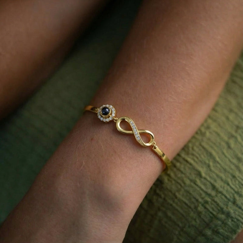 Bracelet en argent 925 doré avec symbole infini et petite pierre noire sertie, style délicat et élégant sur poignet féminin.
