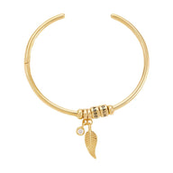 Bracelet ouvert en acier inoxydable doré avec deux anneaux et pendentifs plume et pierre blanche.