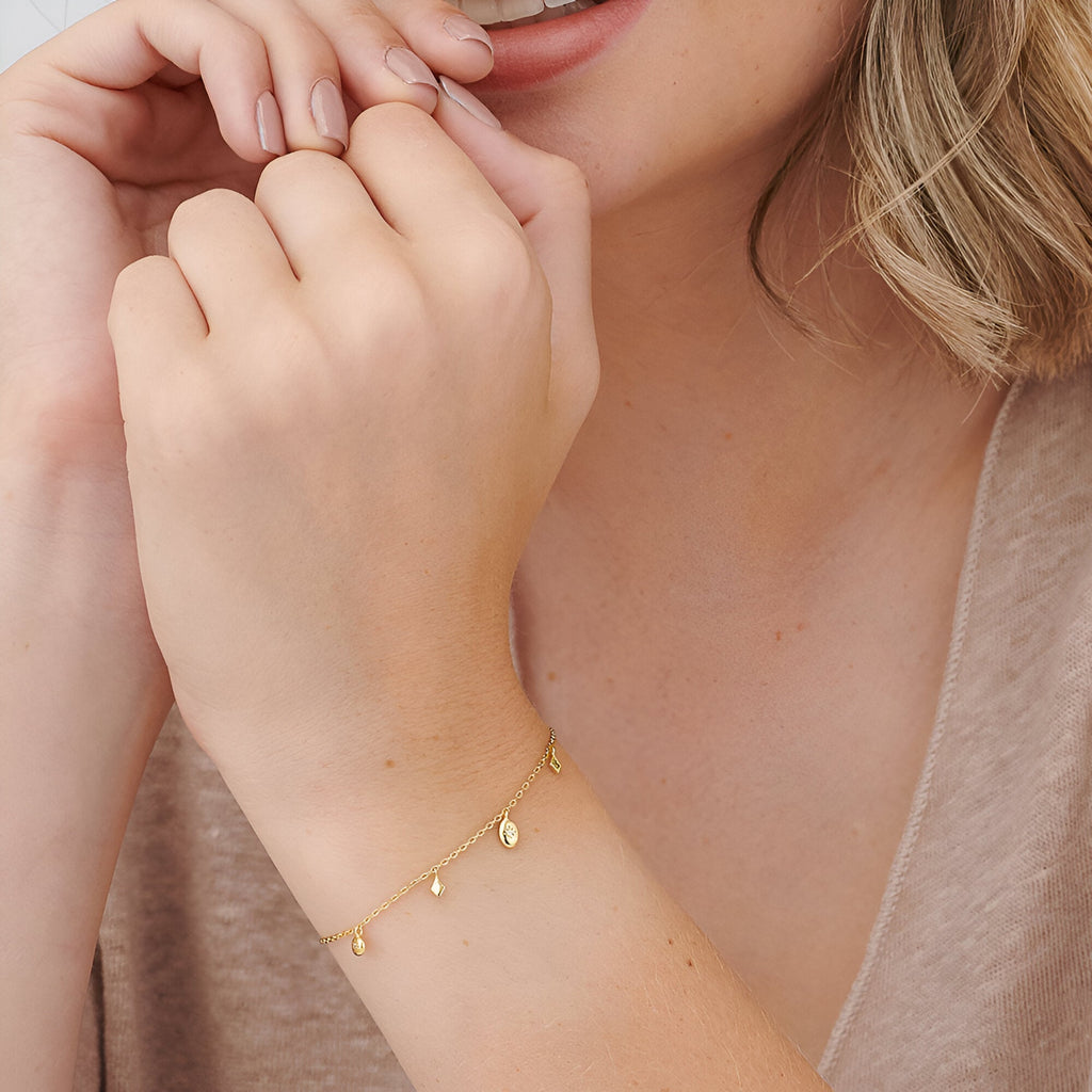 Bracelet délicat en or avec petites breloques ovales brillantes porté au poignet féminin.