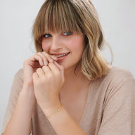 Bracelet fin en argent sterling avec petit pendentif rond gravé, porté au poignet féminin.