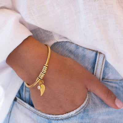 Bracelet quatre anneaux en acier inoxydable doré avec pendentifs plume et anneaux empilés.