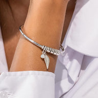 Bracelet en acier inoxydable argenté à quatre anneaux avec pendentif aile et breloque ronde portée sur poignet féminin.
