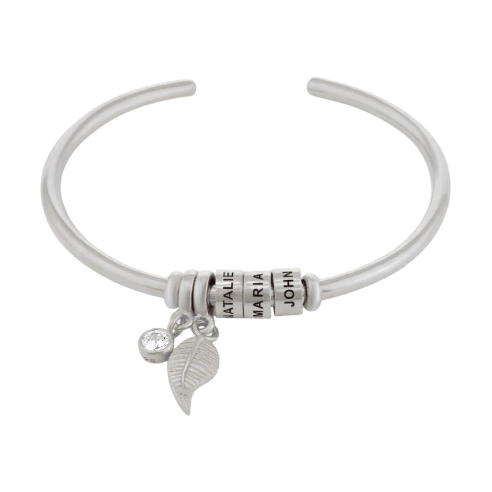 Bracelet ouvert en acier inoxydable argenté avec trois anneaux personnalisables et deux breloques pendantes, dont une.