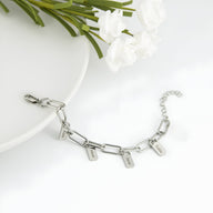 Bracelet femme en acier inoxydable argenté avec trois plaques gravées suspendues sur chaîne à maillons larges.