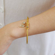 Bracelet fin en acier inoxydable doré avec anneau décoratif et petit pendentif perle sur poignet féminin.