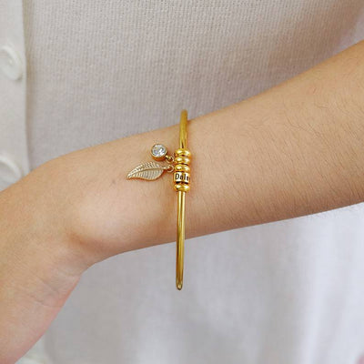 Bracelet fin en acier inoxydable doré avec anneau décoratif et petit pendentif perle sur poignet féminin.