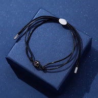 Bracelet à cordon noir réglable en cuir avec pendentif rond argenté lisse sur boîte bleue.