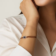 Bracelet cordon en cuir marron clair avec pendentif rond argenté et image cachée, style minimaliste.