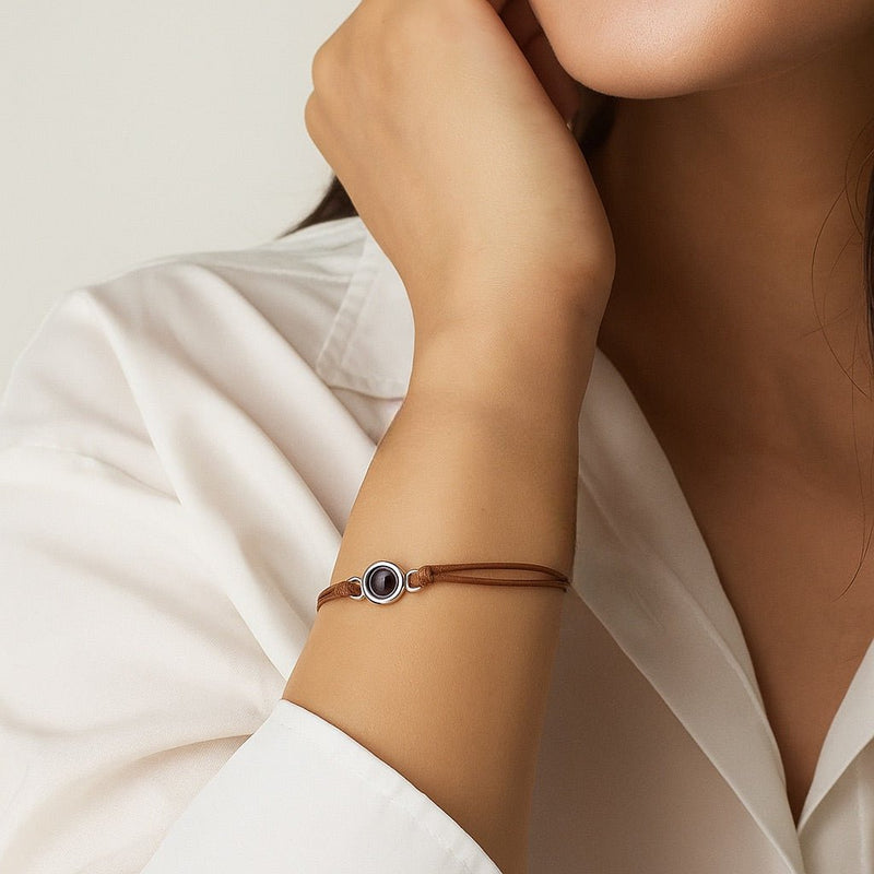 Bracelet cordon en cuir marron clair avec pendentif rond argenté et image cachée, style minimaliste.