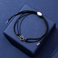 Bracelet à cordon noir en cuir avec pendentif rond en métal argenté, cordon ajustable, design minimaliste et élégant.