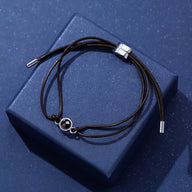 Bracelet à cordon réglable en cuir marron avec pendentif rond argenté à image cachée.