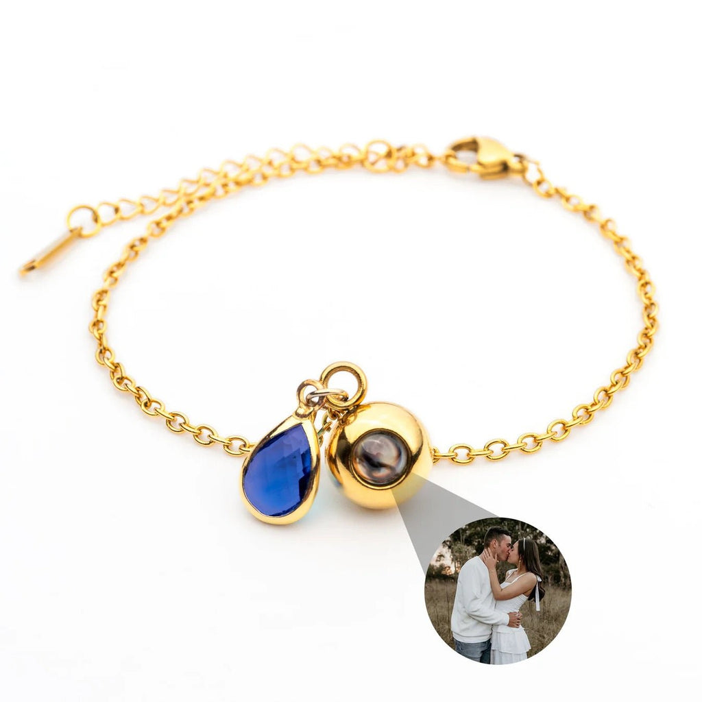 Bracelet chaîne fine dorée en acier inoxydable avec pendentif photo rond et pierre de naissance bleue en forme de goutte.