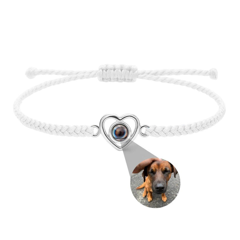 Bracelet blanc tressé avec pendentif cœur en argent projetant une photo d’un chien marron.