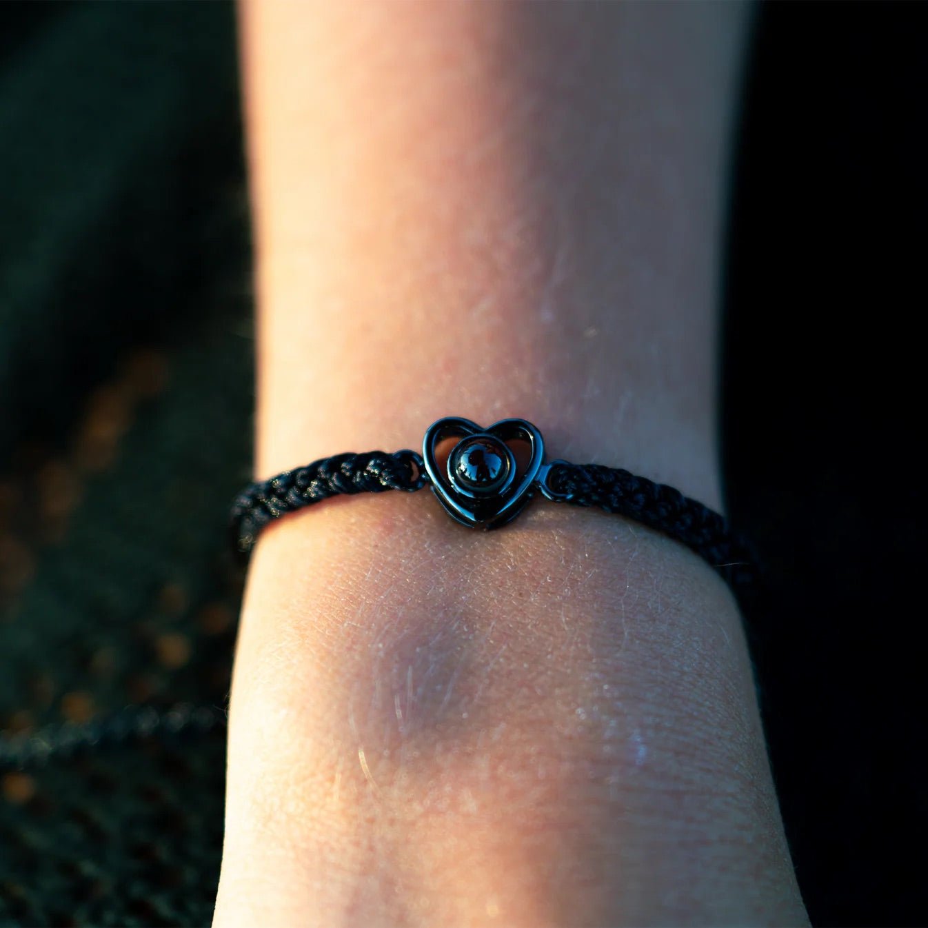 Bracelet noir tressé avec pendentif cœur en argent projetant une photo au centre, style minimaliste.