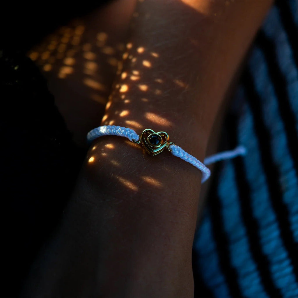 Bracelet fin cordon blanc avec pendentif cœur argenté ajouré au centre du poignet.