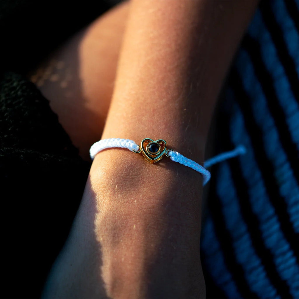 Bracelet blanc en corde tressée avec pendentif cœur en argent doré sur poignet féminin.