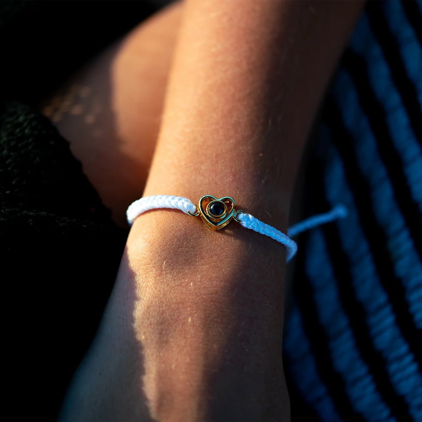 Bracelet blanc en corde tressée avec pendentif cœur en argent doré sur poignet féminin.
