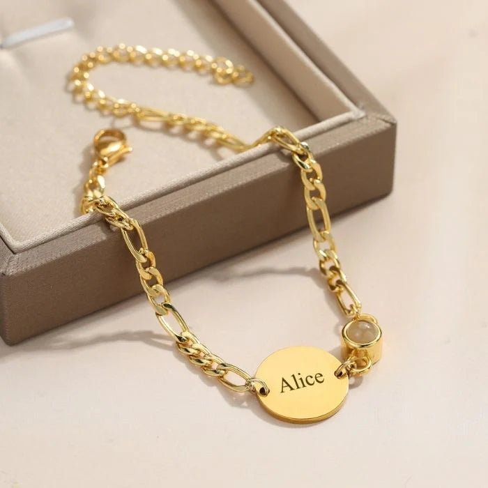 Bracelet doré à mailles figaro avec médaille ovale gravée du prénom Alice et un petit pendentif rond transparent.