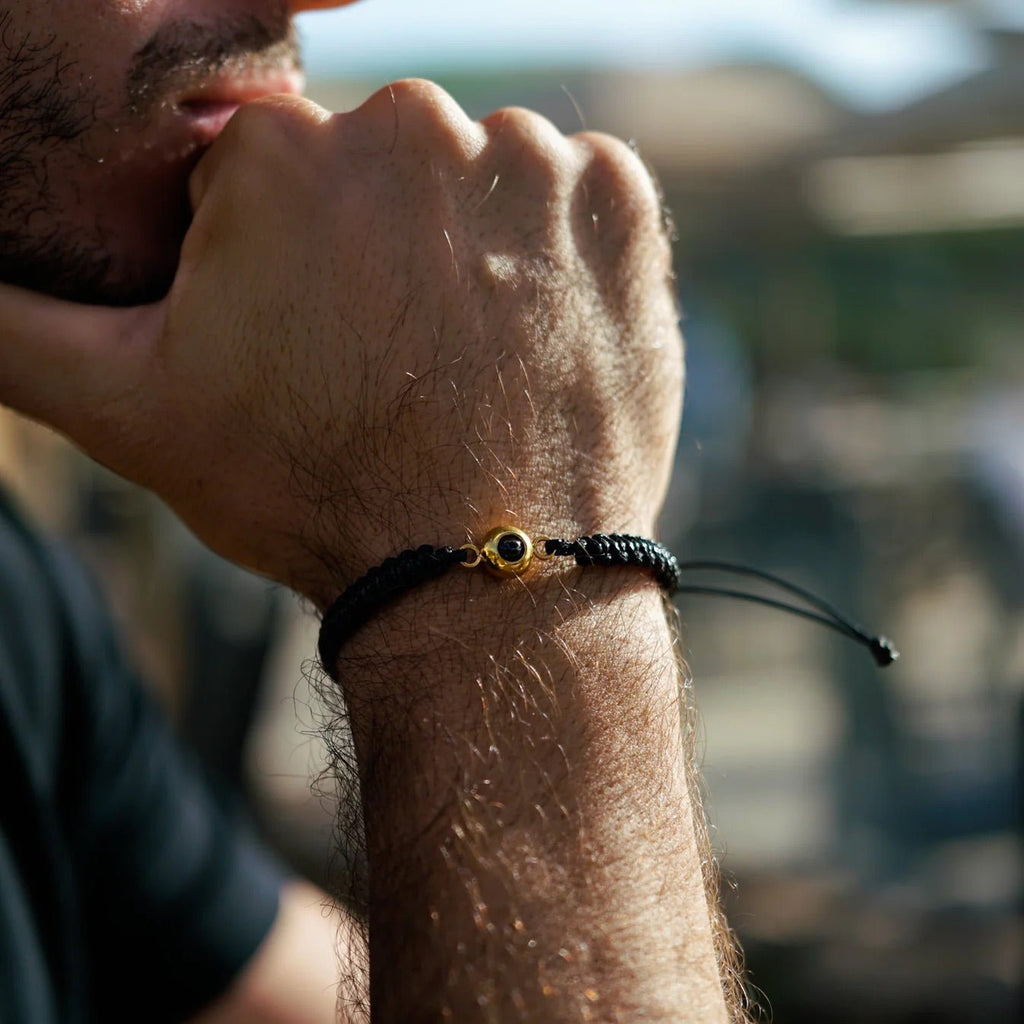 Bracelet corde noire tressée avec médaillon titane rond doré, ajustable, style unisexe.