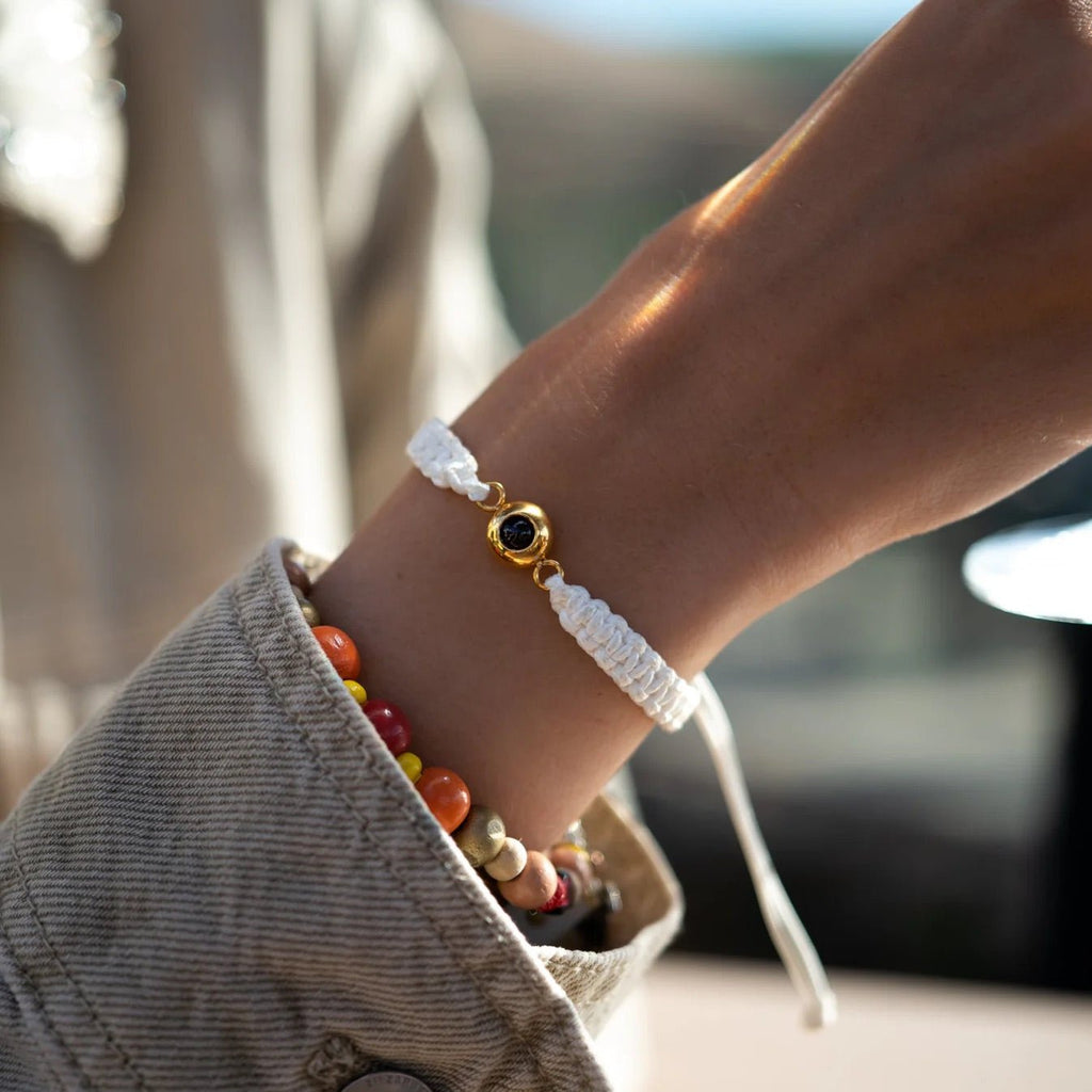 Bracelet fin en corde blanche tressée avec un médaillon rond en titane doré personnalisable, porté au poignet.