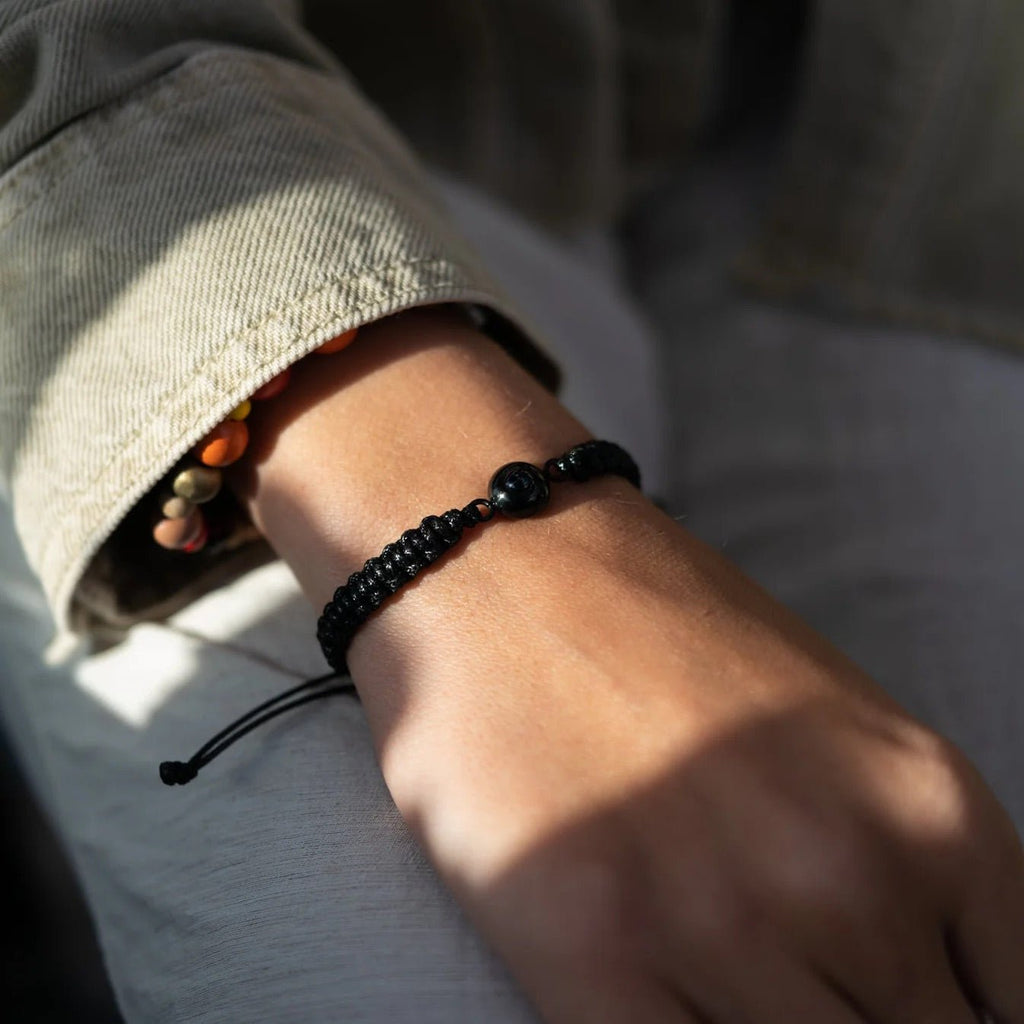 Bracelet en corde noire tressée avec perle centrale en titane noir mat, style minimaliste unisexe.