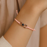Bracelet fin en corde rose clair avec détail infini en titane rose et perle noire centrale.