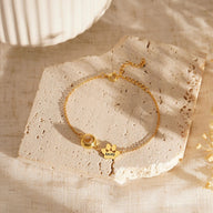 Bracelet personnalisé or avec deux plaquettes à graver en acier inoxydable modèle Cliff posé sur pierre beige.