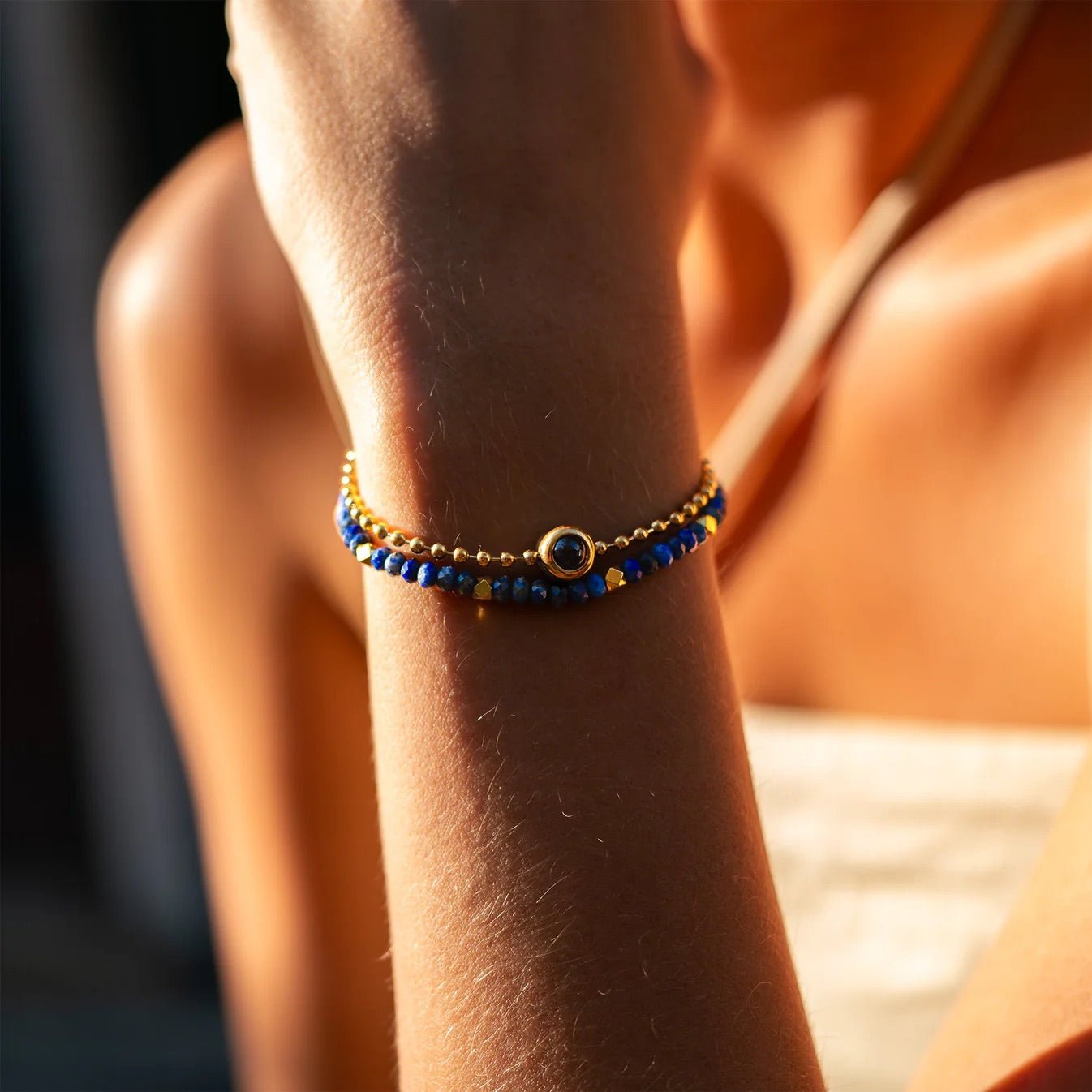 Bracelet double rang en pierres naturelles bleues avec perle centrale dorée sur poignet féminin.