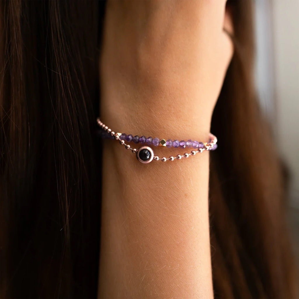 Bracelet double rang en pierres naturelles violettes avec pendentif photo rond argenté sur poignet féminin.