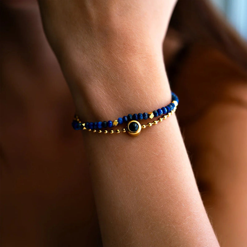 Bracelet double rang en pierres naturelles bleues et perles dorées avec médaille centrale noire et dorée.