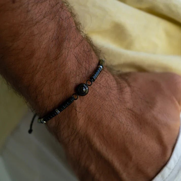 Bracelet ajustable en pierres heishi noires naturelles avec perle centrale ronde en pierre lisse sur poignet masculin.