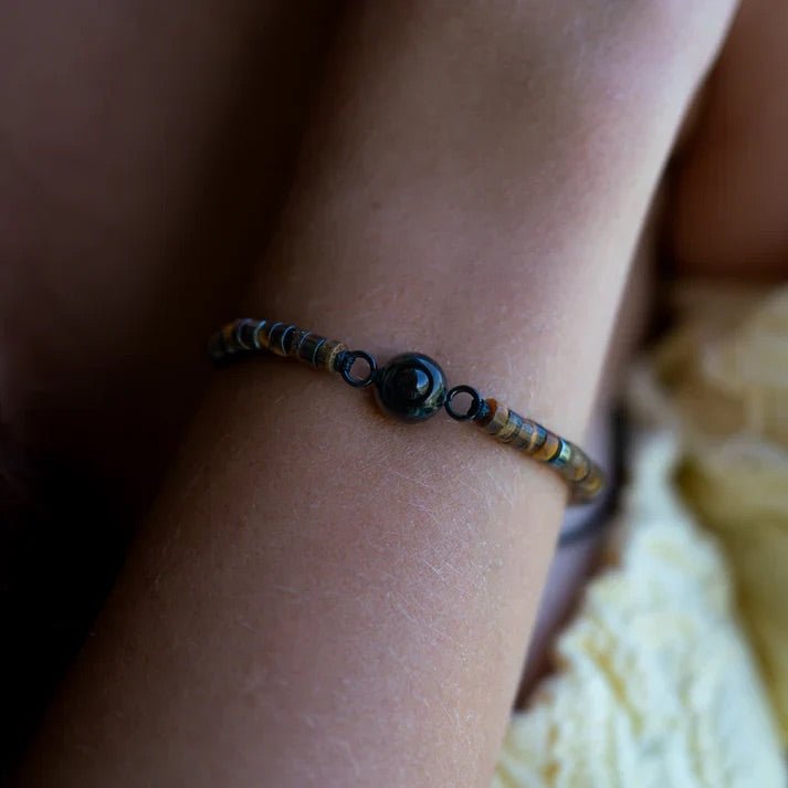 Bracelet fin en pierres heishi multicolores avec perle centrale noire lisse sur poignet féminin.