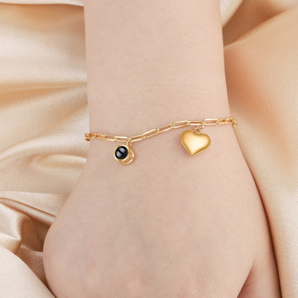 Bracelet chaîne en titane or avec pendentifs cœur et médaillon photo rond sur poignet féminin.