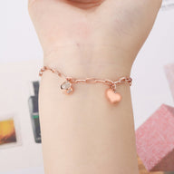 Bracelet en titane or rosé avec chaîne maille allongée et charms cœur et médaillon rond gravés.