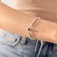 Bracelet photo personnalisé en titane avec chaîne à maillons ronds argentés et pendentif rond noir sur poignet féminin.
