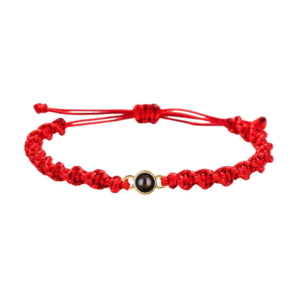 Bracelet tressé en nylon rouge avec fermoir coulissant et médaillon noir circulaire au centre.