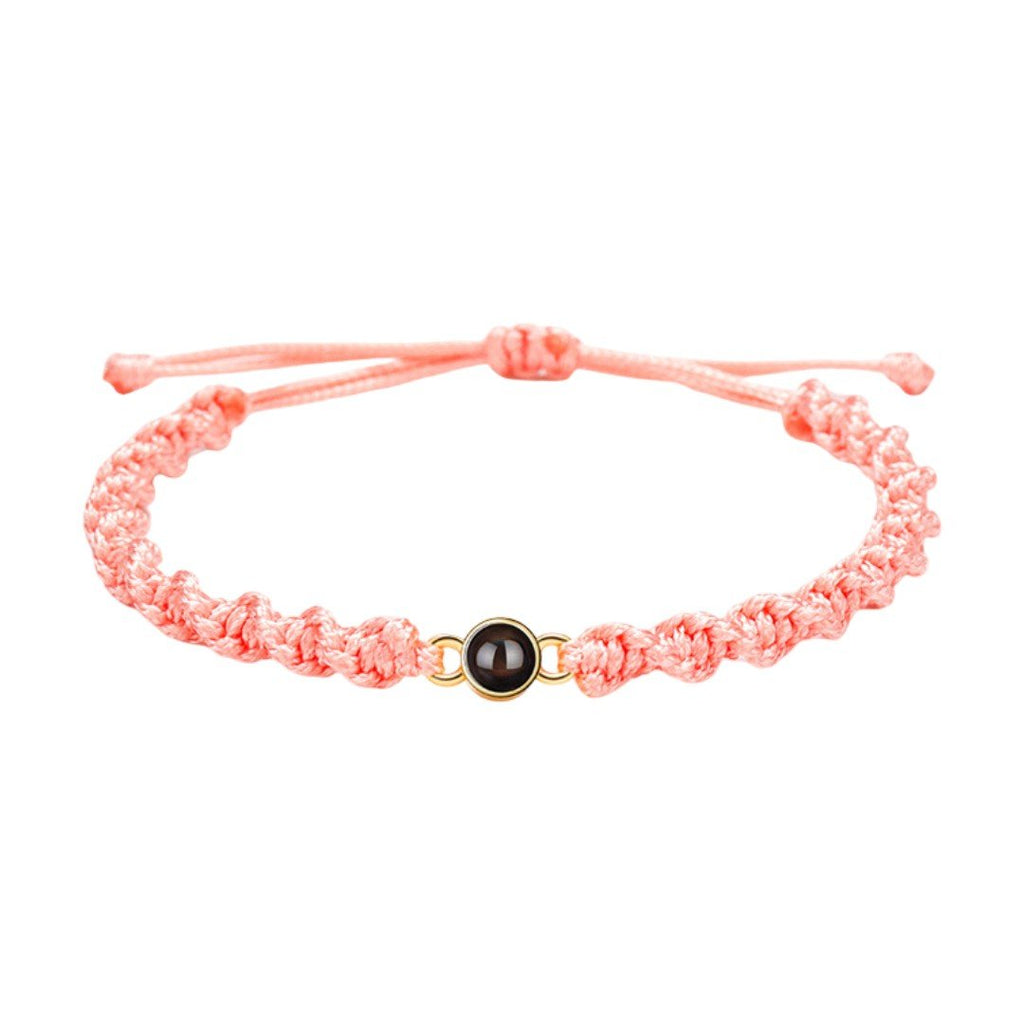 Bracelet tressé en nylon saumon avec fermoir coulissant et médaillon rond noir au centre.