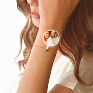 Bracelet fin en acier inoxydable finition or avec pendentif circulaire personnalisable photo, porté au poignet féminin.
