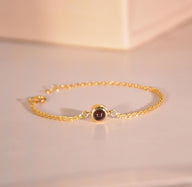 Bracelet fin en acier inoxydable doré avec pendentif rond en projection lumineuse noire, design élégant et minimaliste.